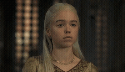A Woman With Blonde Hair And A Gold Necklace Looks At The Camera GIF