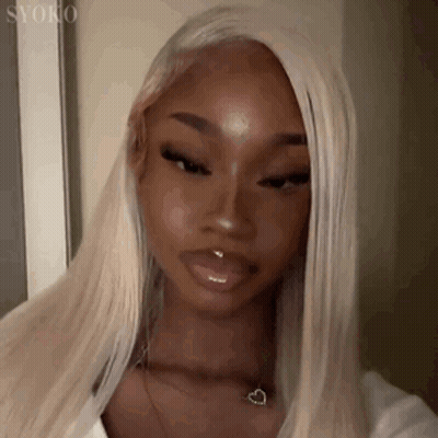 A Woman With Blonde Hair And A Nose Ring Is Wearing A White Shirt And A Heart Necklace . GIF
