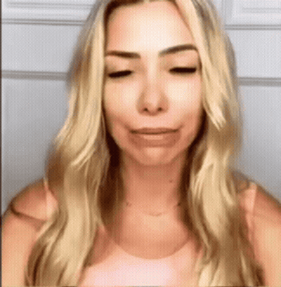 A Woman With Blonde Hair And A Pink Shirt Is Making A Funny Face . GIF
