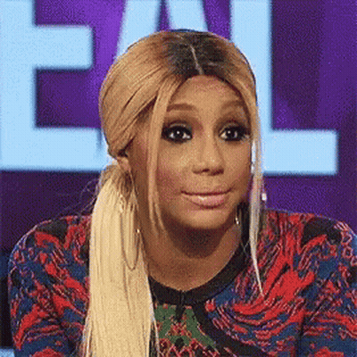 A Woman With Blonde Hair And A Ponytail Is Making A Funny Face While Sitting In Front Of A Sign That Says Call GIF