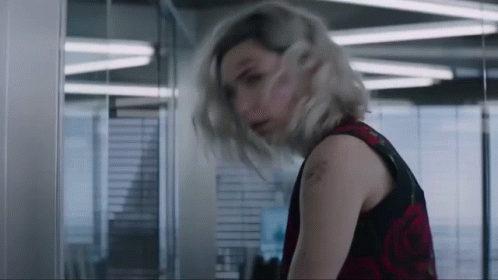 A Woman With Blonde Hair And A Tattoo On Her Arm Is Standing In A Room GIF