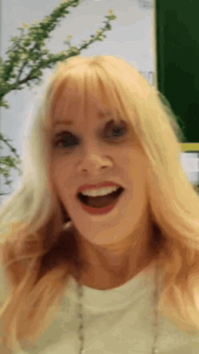A Woman With Blonde Hair And A White Shirt Is Smiling GIF
