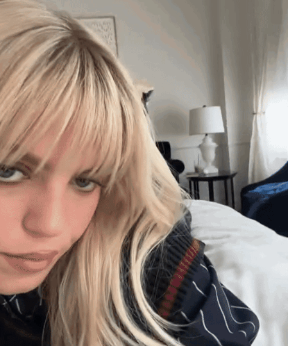 A Woman With Blonde Hair And Bangs Is Laying On A Bed GIF