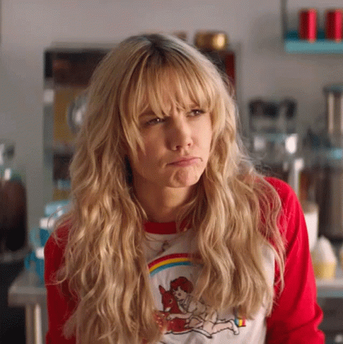 A Woman With Blonde Hair And Bangs Is Wearing A Red Shirt And Making A Face . GIF