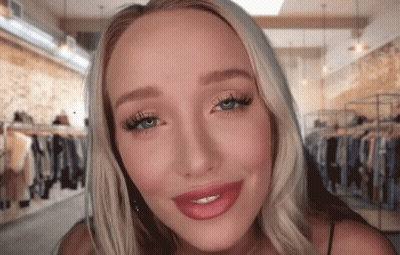 A Woman With Blonde Hair And Blue Eyes Is Smiling In Front Of A Clothing Store GIF