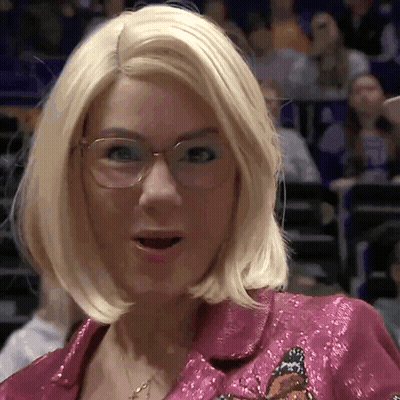 A Woman With Blonde Hair And Glasses Is Wearing A Pink Jacket With A Butterfly Embroidered On It GIF