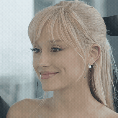 A Woman With Blonde Hair And Pearl Earrings Smiles For The Camera GIF