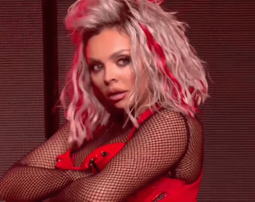 A Woman With Blonde Hair And Red Highlights Is Wearing A Red Top And Fishnet Stockings . GIF