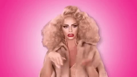 A Woman With Blonde Hair And Red Lipstick Is Making A Peace Sign With Her Hands On A Pink Background . GIF