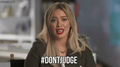 A Woman With Blonde Hair And Red Lipstick Is Sitting In A Chair And Saying `` Don 'T Judge '' . GIF