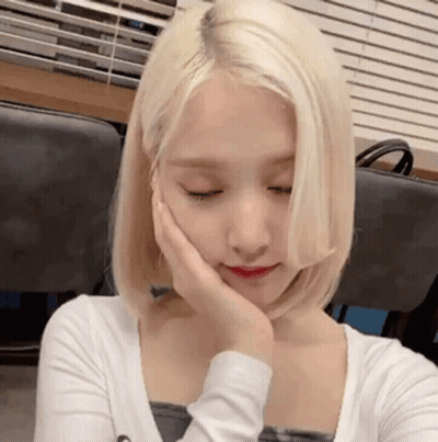 A Woman With Blonde Hair Is Holding Her Hand To Her Face . GIF