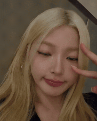 A Woman With Blonde Hair Is Making A Heart With Her Fingers GIF