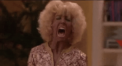 A Woman With Blonde Hair Is Screaming With Her Mouth Wide Open In A Room . GIF