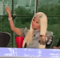 A Woman With Blonde Hair Is Sitting At A Table Giving A Middle Finger GIF