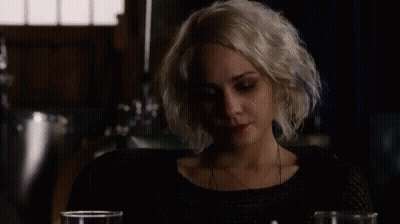 A Woman With Blonde Hair Is Sitting At A Table With Two Glasses Of Wine . GIF
