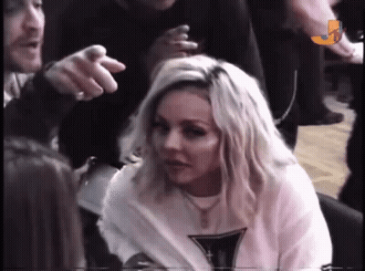 A Woman With Blonde Hair Is Sitting In A Crowd While A Man Points At Her . GIF