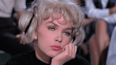 A Woman With Blonde Hair Is Sitting In A Theatre With Her Hand On Her Chin . GIF