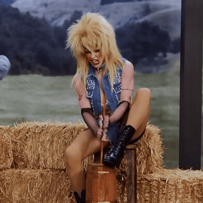 A Woman With Blonde Hair Is Sitting On A Bale Of Hay Holding A Hammer GIF