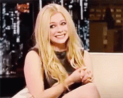 A Woman With Blonde Hair Is Sitting On A Couch Smiling . GIF
