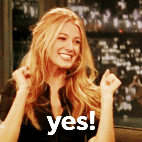A Woman With Blonde Hair Is Smiling And Holding Her Fist Up In The Air With The Words Yes Behind Her GIF