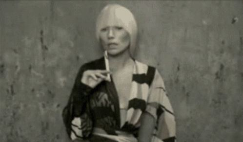 A Woman With Blonde Hair Is Smoking A Cigarette In A Black And White Photo . GIF