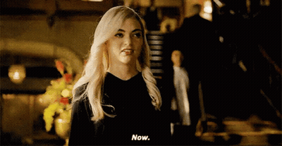 A Woman With Blonde Hair Is Standing In A Dark Room And Talking To A Man . GIF