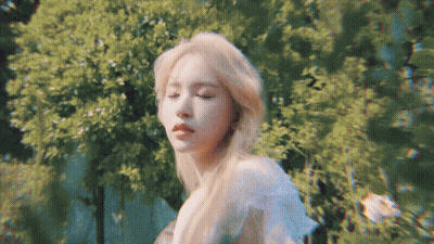 A Woman With Blonde Hair Is Standing In Front Of A Forest . GIF