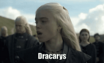 A Woman With Blonde Hair Is Standing In Front Of A Group Of People And The Word Dracarys Is On Her Face . GIF