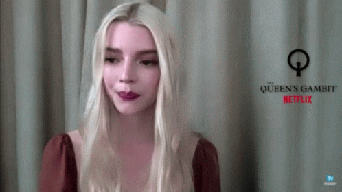 A Woman With Blonde Hair Is Standing In Front Of A Sign That Says Queen 'S Gambit Netflix GIF
