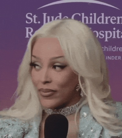 A Woman With Blonde Hair Is Talking Into A Microphone In Front Of A St. Jude Children 'S Hospital Sign GIF