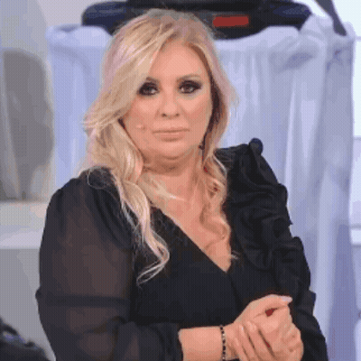 A Woman With Blonde Hair Is Wearing A Black Ruffled Top And A Black Bracelet On Her Wrist . GIF