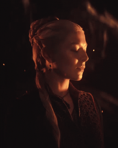 A Woman With Blonde Hair Is Wearing A Black Vest And A Necklace GIF