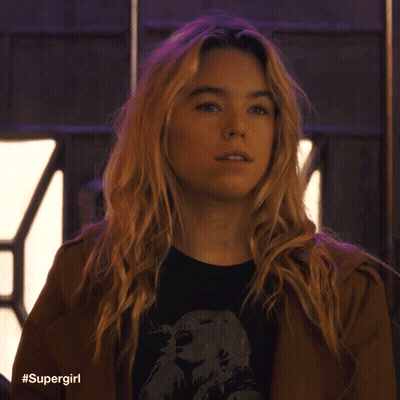 A Woman With Blonde Hair Is Wearing A Brown Jacket And A Black Shirt With A Picture Of An Eagle On It . GIF