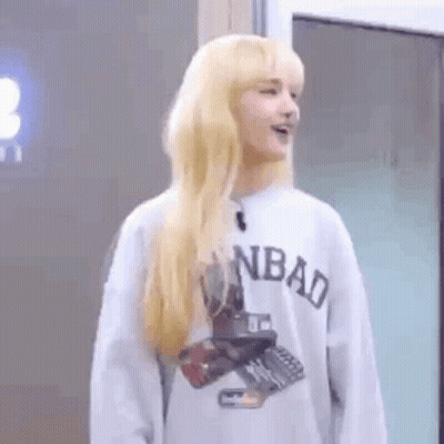 A Woman With Blonde Hair Is Wearing A Gray Sweatshirt And Standing In Front Of A Door . GIF