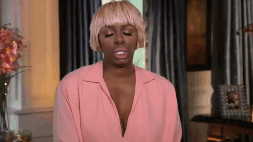 A Woman With Blonde Hair Is Wearing A Pink Shirt And Making A Funny Face In A Living Room . GIF