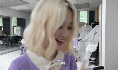A Woman With Blonde Hair Is Wearing A Purple Sweater And A White Shirt . GIF
