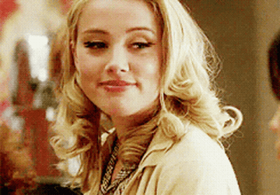 A Woman With Blonde Hair Is Wearing A Tan Jacket And A Necklace GIF