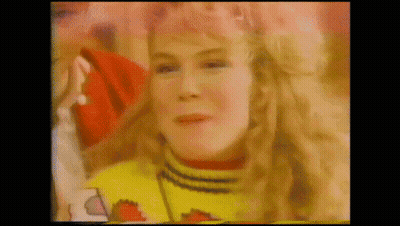 A Woman With Blonde Hair Is Wearing A Yellow Sweater And A Red Hat . GIF