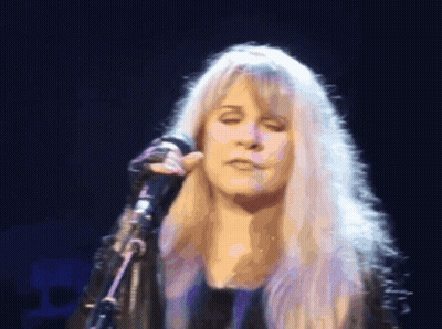 A Woman With Blonde Hair Singing Into A Microphone With Her Eyes Closed GIF