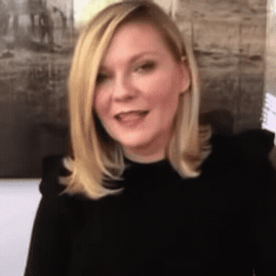 A Woman With Blonde Hair Wearing A Black Shirt Is Smiling . GIF