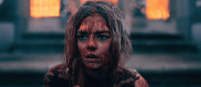A Woman With Blood On Her Face Is Sitting In Front Of A Fire . GIF