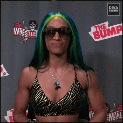 A Woman With Blue And Green Hair Is Standing In Front Of A Sign That Says Wrestle The Bump GIF