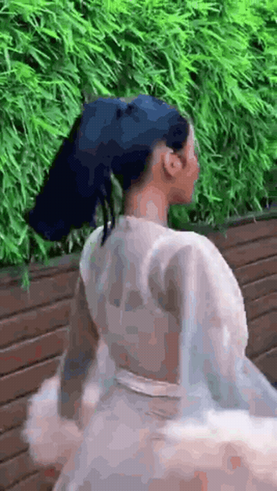 A Woman With Blue Hair And A White Dress Is Standing In Front Of A Wooden Fence . GIF
