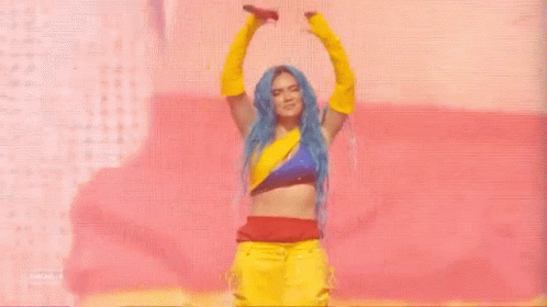 A Woman With Blue Hair And Yellow Gloves Is Dancing On A Stage With A Microphone . GIF
