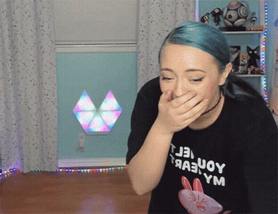 A Woman With Blue Hair Is Covering Her Mouth With Her Hand And Wearing A Black T-Shirt With A Rabbit On It GIF