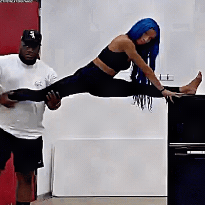 A Woman With Blue Hair Is Doing A Split On A Table While A Man Holds Her Legs . GIF