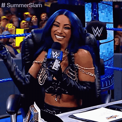 A Woman With Blue Hair Is Holding A Microphone And Smiling While Sitting In A Chair . GIF