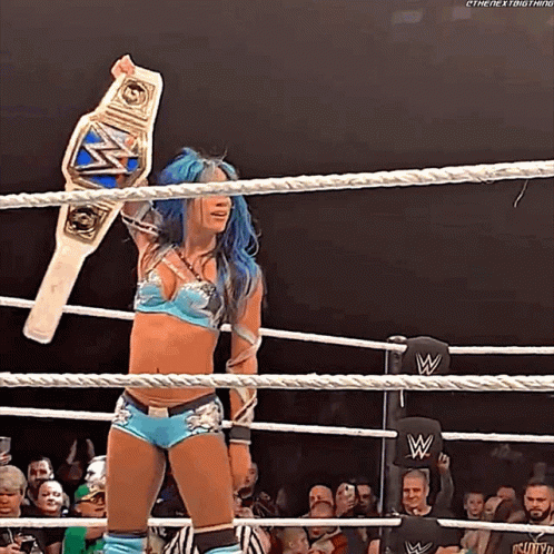 A Woman With Blue Hair Is Holding A Wrestling Championship Belt In A Ring GIF
