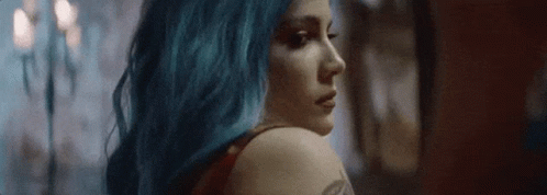 A Woman With Blue Hair Is Looking Over Her Shoulder At The Camera . GIF