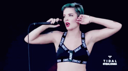 A Woman With Blue Hair Is Singing Into A Microphone While Wearing A Bra That Says Sweat Crew GIF
